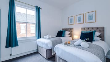 A hotel room with two beds, a window with curtains, a radiator, and three framed pictures on the wall.