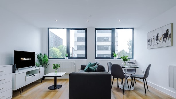 A modern living room with a flat-screen TV, a sofa, a dining table with chairs, and large windows. - NEW Stylish Apartment Amazing Location Sleeps 4 (Manchester)