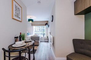 A narrow room with a dining table, chairs, a sofa, a bed, a window, and a TV. - NEW Stunning Studio in the City-centre Sleeps 2 (Chester)