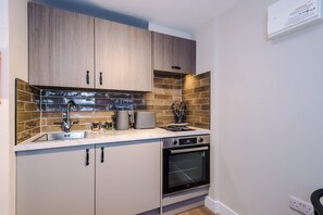 A compact kitchen with wooden cabinets, a stainless steel sink, a built-in oven, and a tiled backsplash. - NEW Stunning Studio in the City-centre Sleeps 2 (Chester)