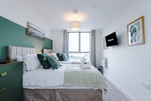 A bedroom with a bed, a nightstand, a TV, and a window with curtains. - NEW Pristine 2-bed Flat Great Location Sleeps 6 (Liverpool)