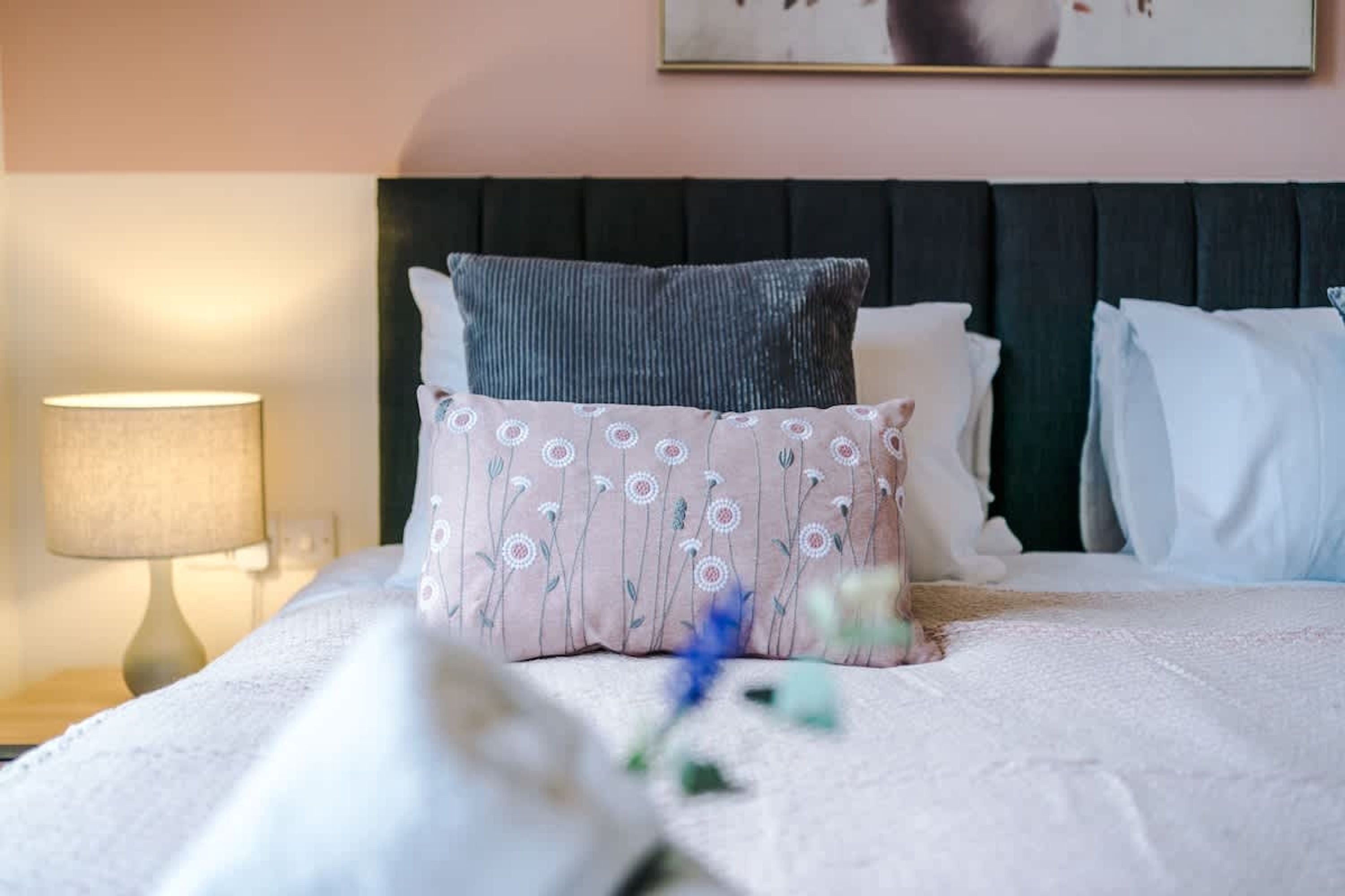 A neatly made bed with a pillow, a bedside lamp, and a framed picture on the wall.