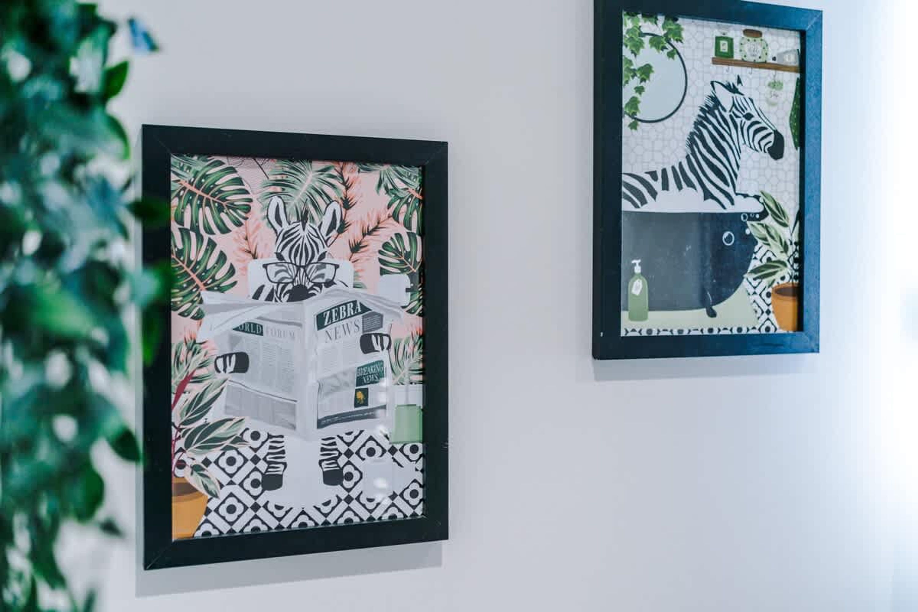 Zwei gerahmte Kunstwerke an einer Wand, eines zeigt ein Zebra und das andere ein Zebra sowie eine Flasche.