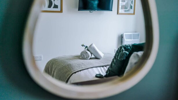 A bedroom with a bed, a TV mounted on the wall, and a wall-mounted air conditioner. - NEW Pristine 2-bed Flat Great Location Sleeps 6 (Liverpool)