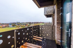 Varanda com vista para o horizonte urbano, porta de vidro e guarda-corpo de metal com detalhes circulares.