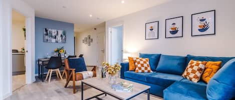 Ein modernes Wohnzimmer mit einem blauen Sofa, einem Couchtisch und einem Essbereich mit Stühlen und einem Tisch.