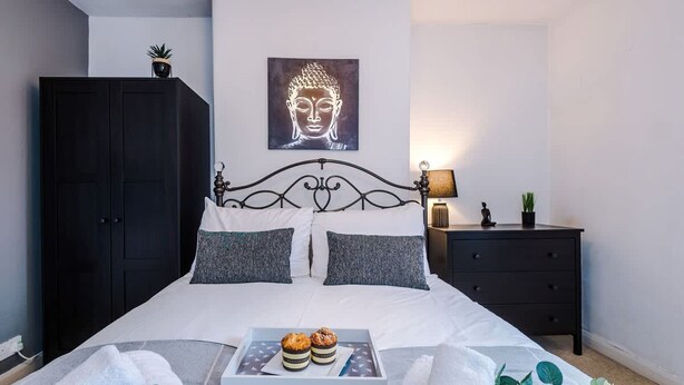 A bedroom with a bed, a nightstand, a dark wardrobe, a Buddha painting, and a tray with pastries. - Stunning Home Amazing Location Great For Groups (Chester)