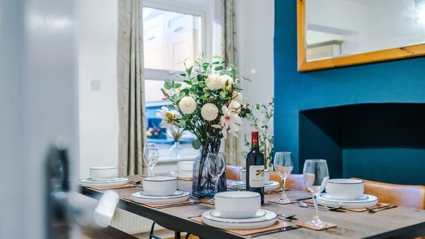 Une table à manger dressée avec des assiettes, des verres et un vase de fleurs.