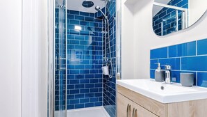 Un baño con azulejos azules, cabina de ducha de vidrio, lavamanos blanco y armarios de madera.