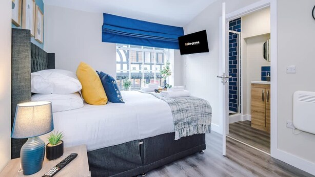 Un dormitorio moderno con cama, mesita de noche, lámpara y televisor fijado a la pared.