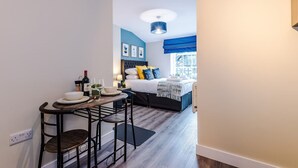 Habitación de hotel pequeña con cama, mesita de noche y una zona de comedor compacta con taburetes.