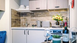 Una cocina moderna con salpicadero de azulejos, armarios blancos y una encimera con cafetera, tostadora y un florero con flores.