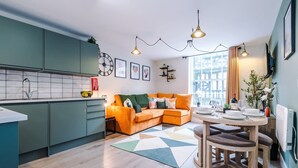 A modern kitchen with teal cabinets, a dining area with a wooden table and chairs, and a cozy orange sofa. - NEW Stylish 1-bed Flat Great Location Sleeps 4 (Chester)
