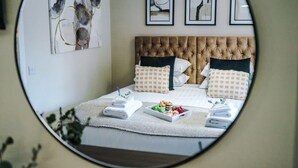 A bedroom with a tufted headboard, a bed with multiple pillows, a tray of snacks, and a neatly folded towel. - NEW Stylish 1-bed Flat Great Location Sleeps 4 (Chester)