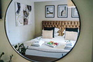 Camera da letto con testiera trapuntata, un letto con numerosi cuscini, un vassoio con degli snack e un asciugamano piegato con cura.