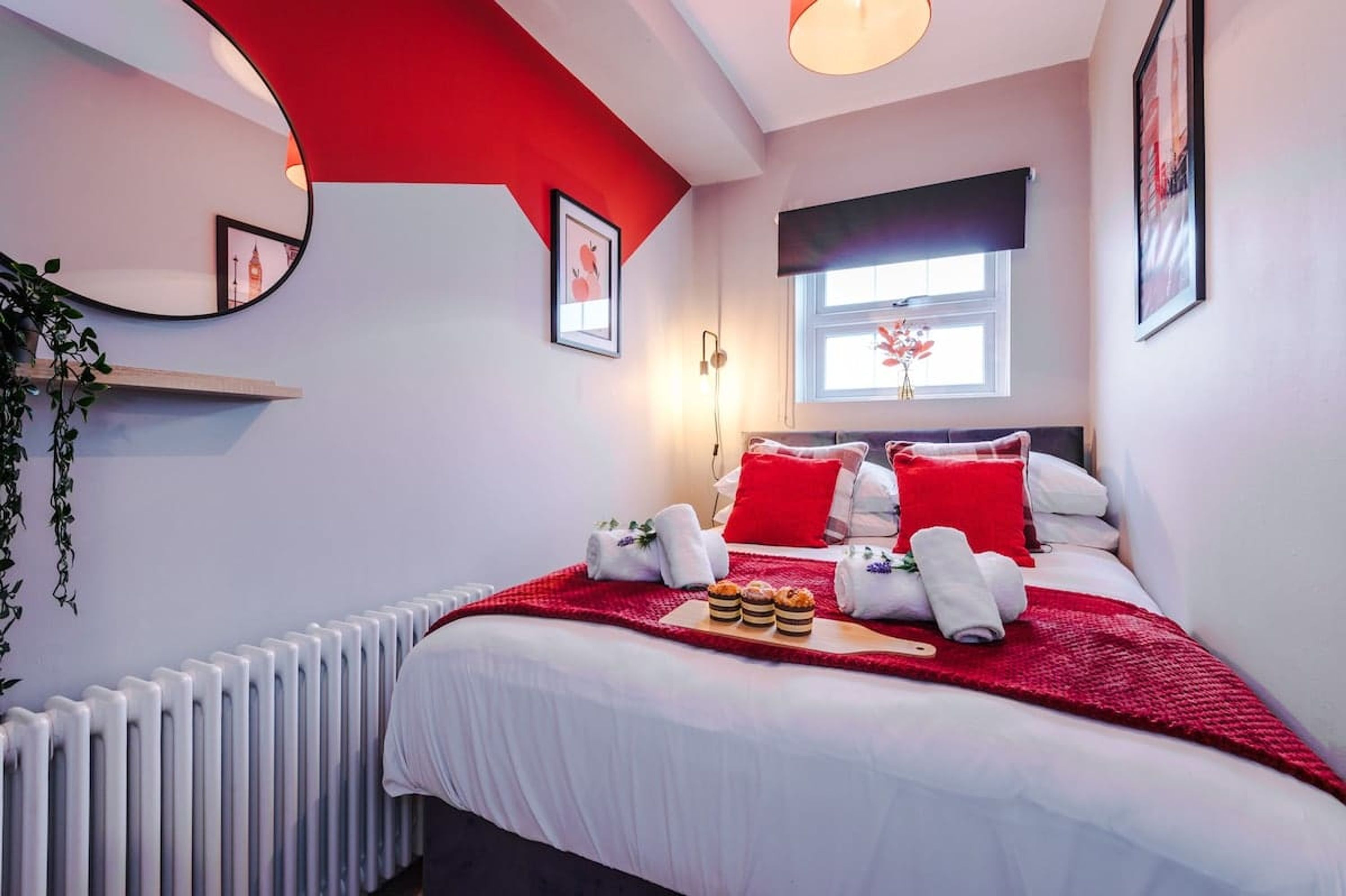 A hotel room with a bed, red accents, a window, and a radiator.