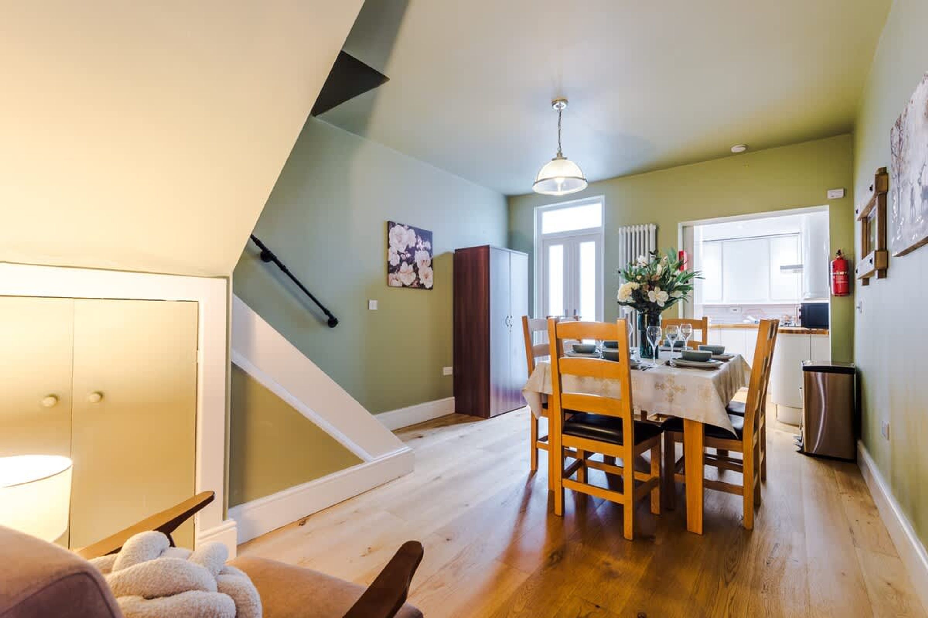 A dining area with a table set for four, a staircase, and a kitchen in the background.