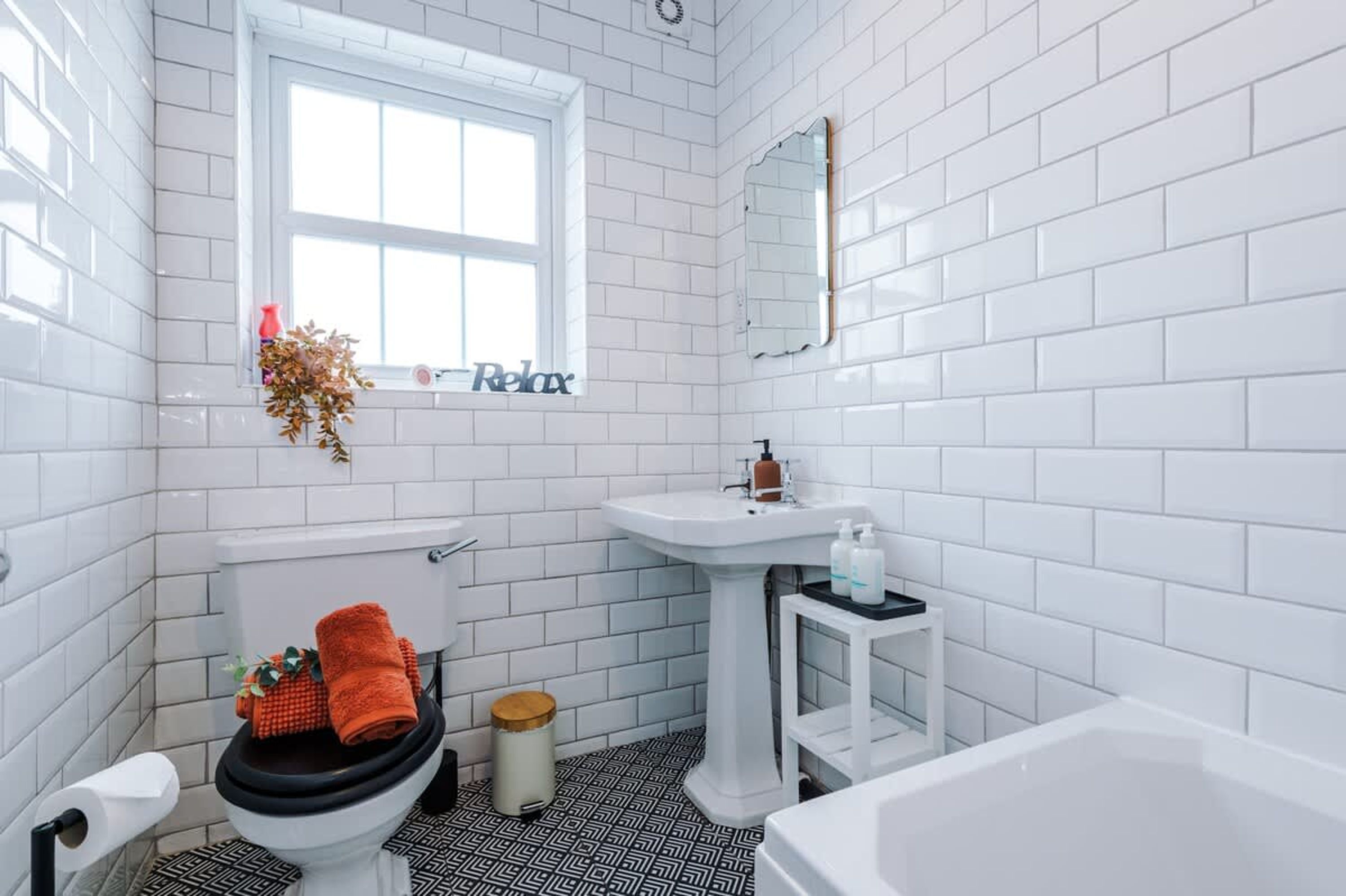 A bathroom with white tiled walls, a window, a toilet, a sink, and a bathtub.