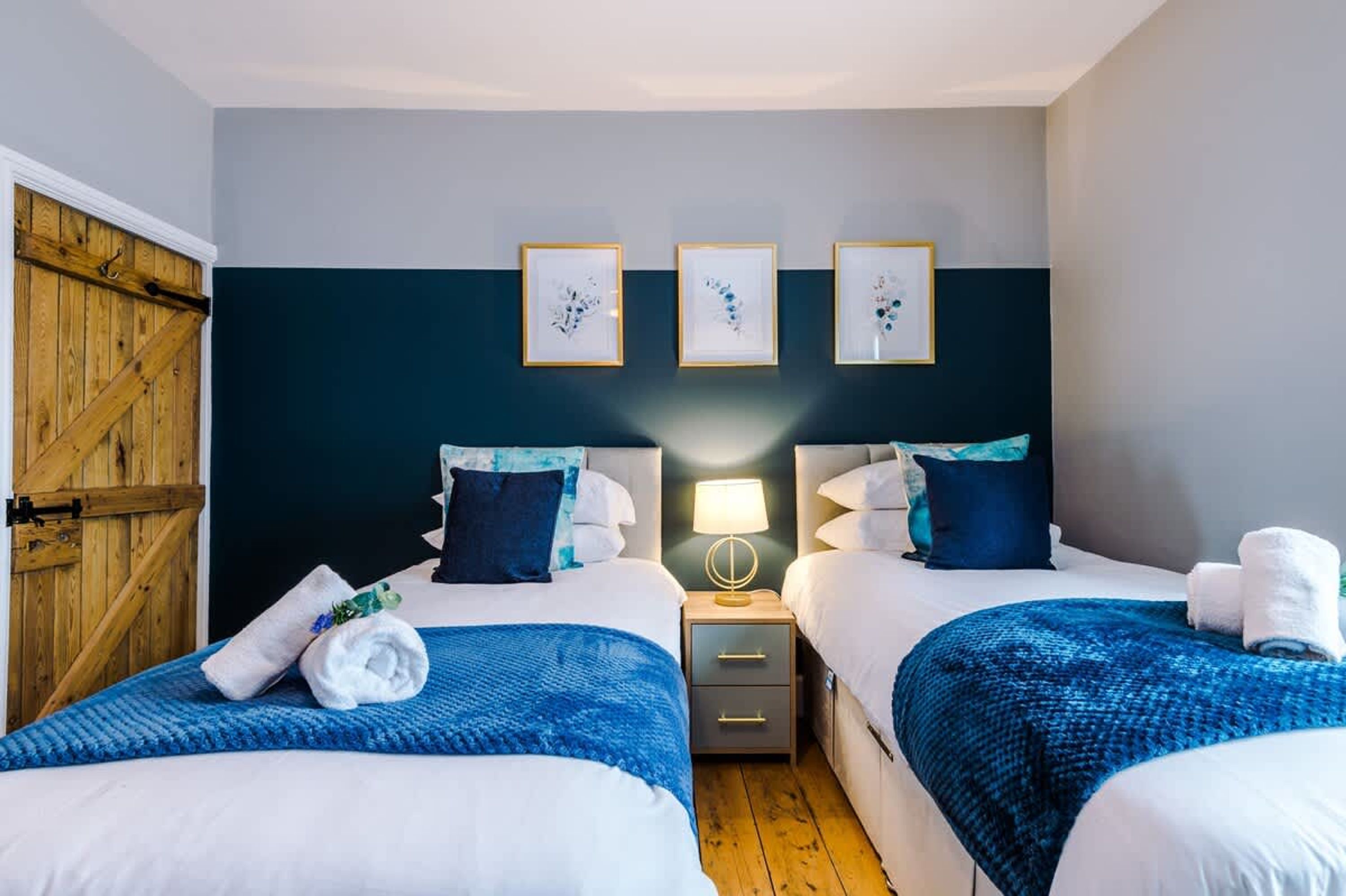 A hotel room with two beds, a wooden door, and three framed pictures on the wall.