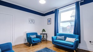A room with a blue sofa, a blue armchair, a small table with a plant, and a window with blue curtains. - Charming Home Perfectly Located in Chester (Chester)