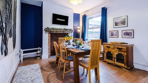 A dining area with a brick fireplace, wooden chairs, a table set for four, and a blue pendant light. - Charming Home Perfectly Located in Chester (Chester)