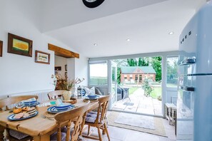 A dining area with a wooden table, chairs, and a view of a house through glass doors. - NEW Stunning Cottage Ideal for Families Groups (Crewe)