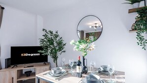Ett modernt matområde med en TV, ett matbord dukat med tallrikar, glas och en vinflaska.