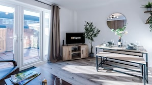 Ett modernt vardagsrum med en tv, ett matbord och ett stort fönster med gardiner.