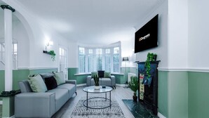 Una sala de estar moderna con un sofá gris, una mesa de centro de vidrio, una chimenea y un televisor montado en la pared.