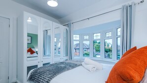 Un dormitorio con una cama grande, un armario y una ventana con vistas a casas.