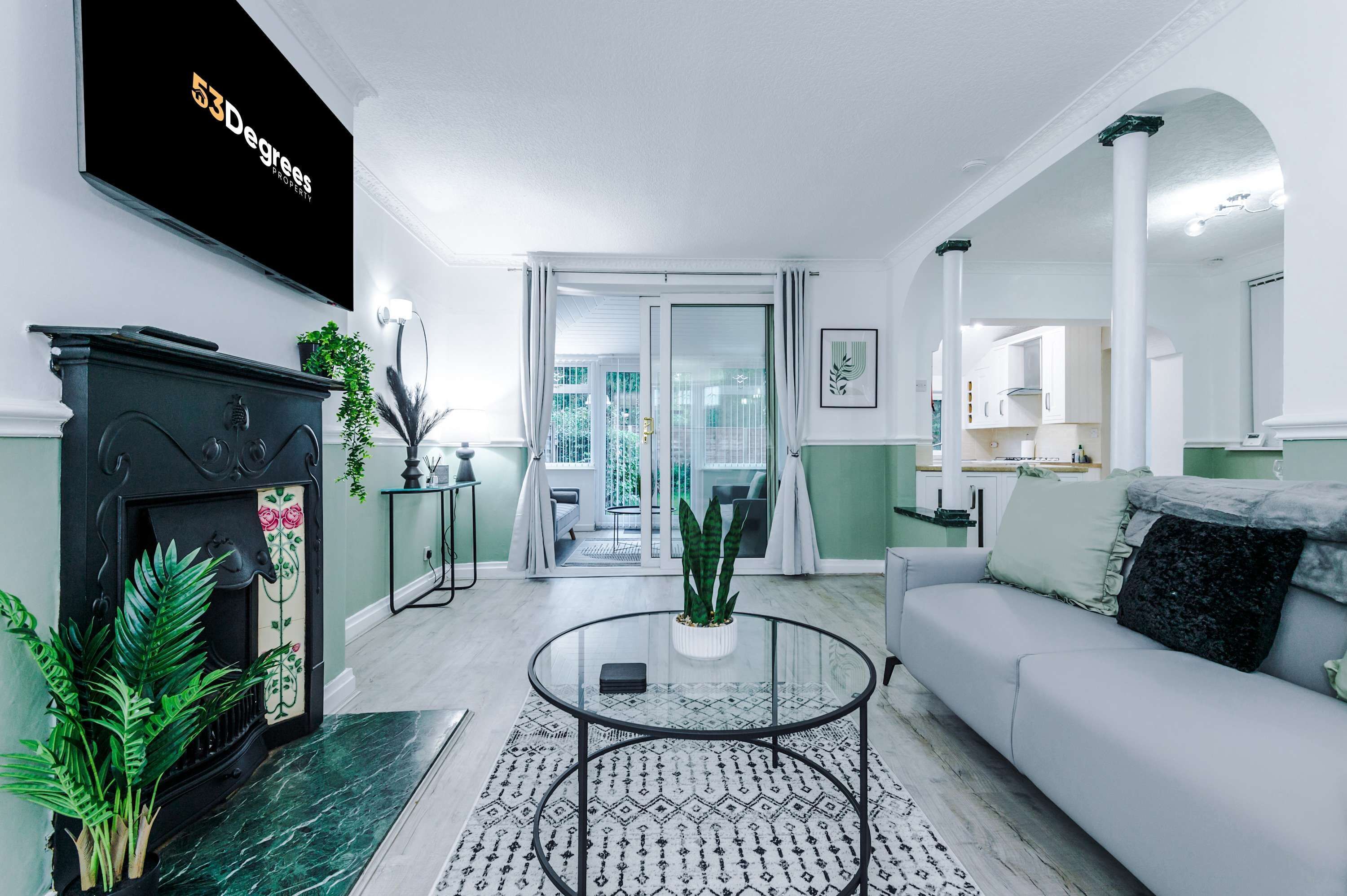 A modern living room with a fireplace, a glass coffee table, a sofa, and a view to the outside.