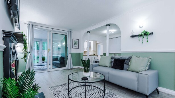 Una sala de estar moderna con una mesa de centro de vidrio, un sofá gris y un gran ventanal corredero que da a un balcón.