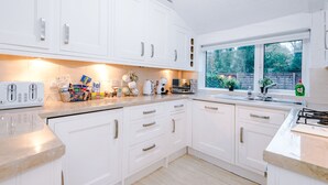 Una cocina moderna con armarios blancos, una encimera con diversos electrodomésticos y una ventana con vistas al verdor.