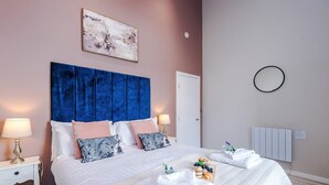 A neatly made bed with a blue headboard, white bedding, and a bedside table with a lamp. - City Centre Flat Perfect for Groups Weekends (Liverpool)