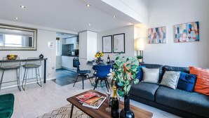 A modern living room with a sofa, a dining table, and a kitchen in the background. - City Centre Flat Perfect for Groups Weekends (Liverpool)