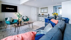 A modern living room with a sofa, chairs, a coffee table, and a TV. There's a dining area with a table and chairs. - City Centre Flat Perfect for Groups Weekends (Liverpool)