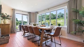 Comedor con una mesa preparada para seis personas, ventanas grandes y vista a zonas verdes.