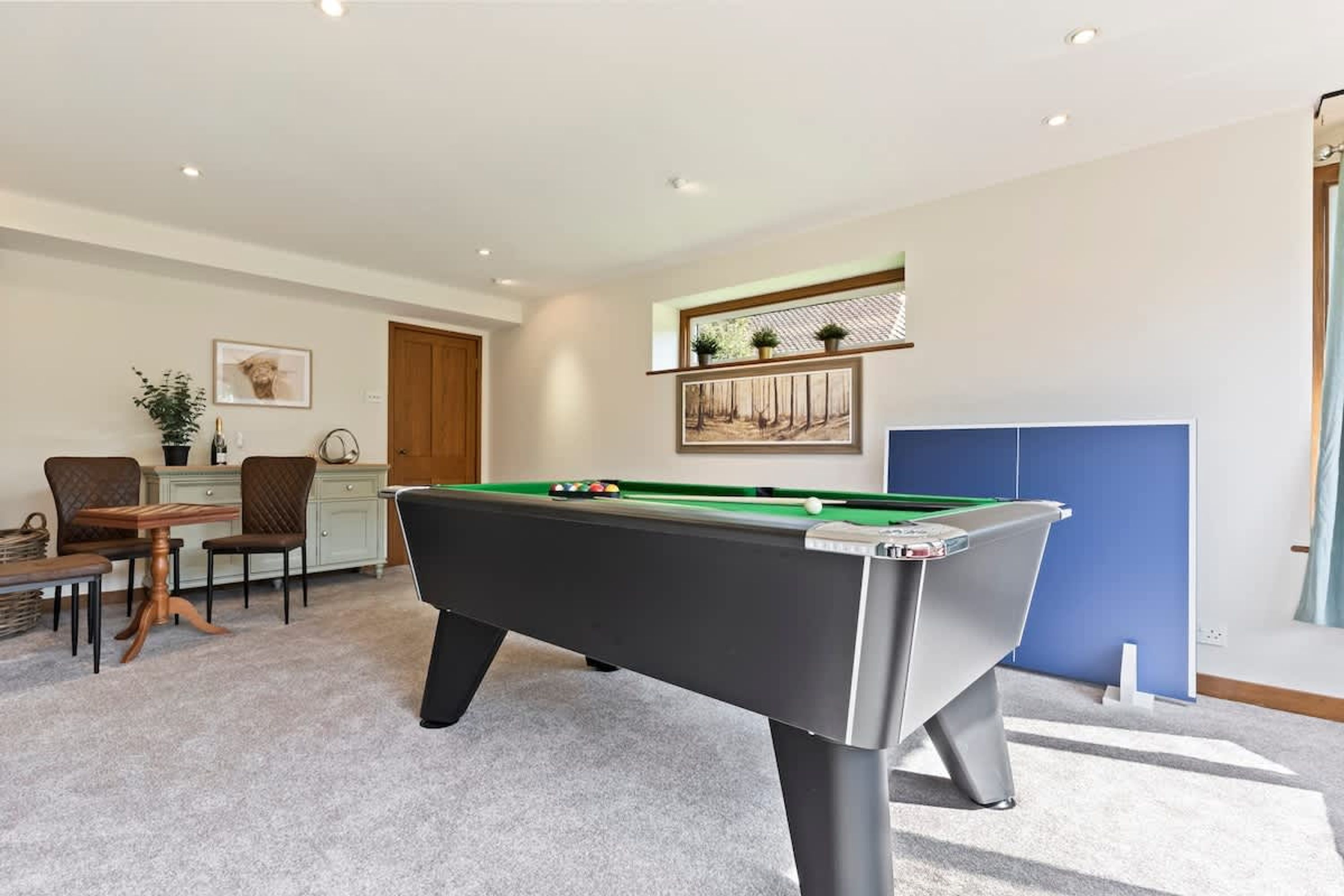 A pool table in a room with a dining area, a cabinet, and a door.