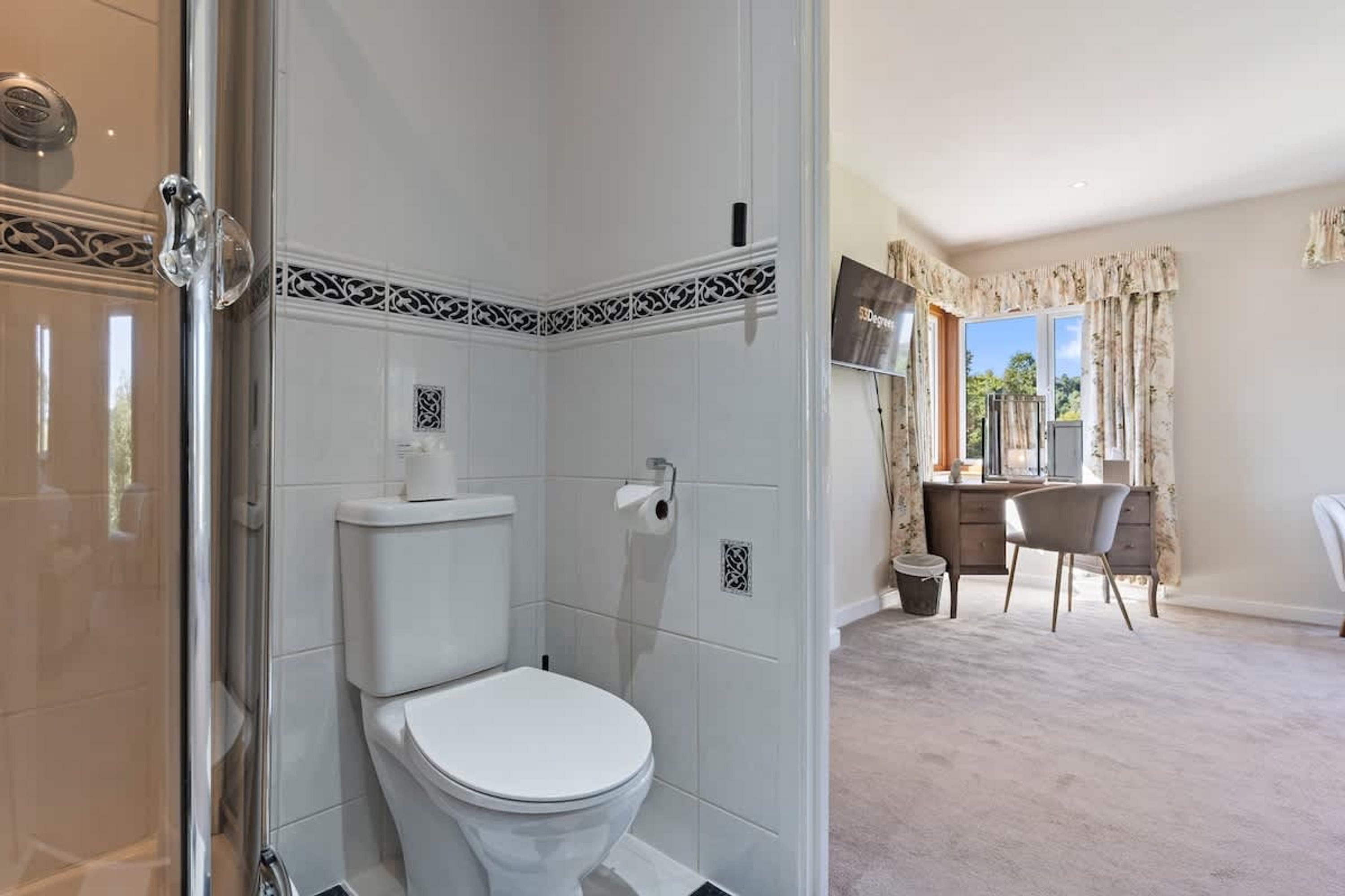 Une salle de bain équipée de toilettes, d’une douche et d’un coin bureau avec une chaise et un téléviseur.