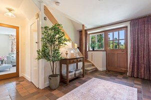 Una escalera que lleva a un segundo piso, una consola de madera con una planta, una puerta con un ventanal y una alfombra estampada.