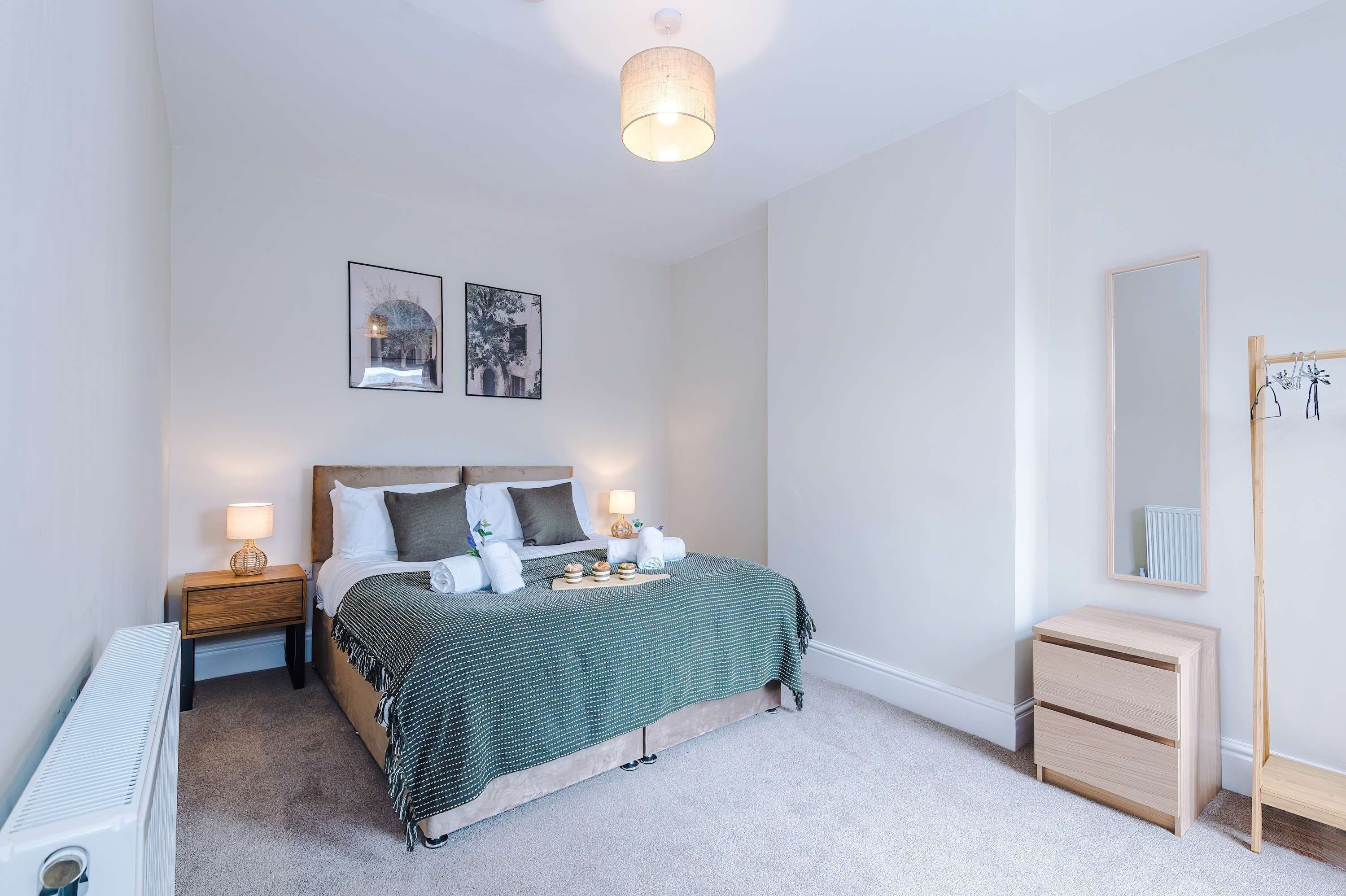 Un dormitorio con cama, mesitas de noche, cómoda, radiador y espejo.