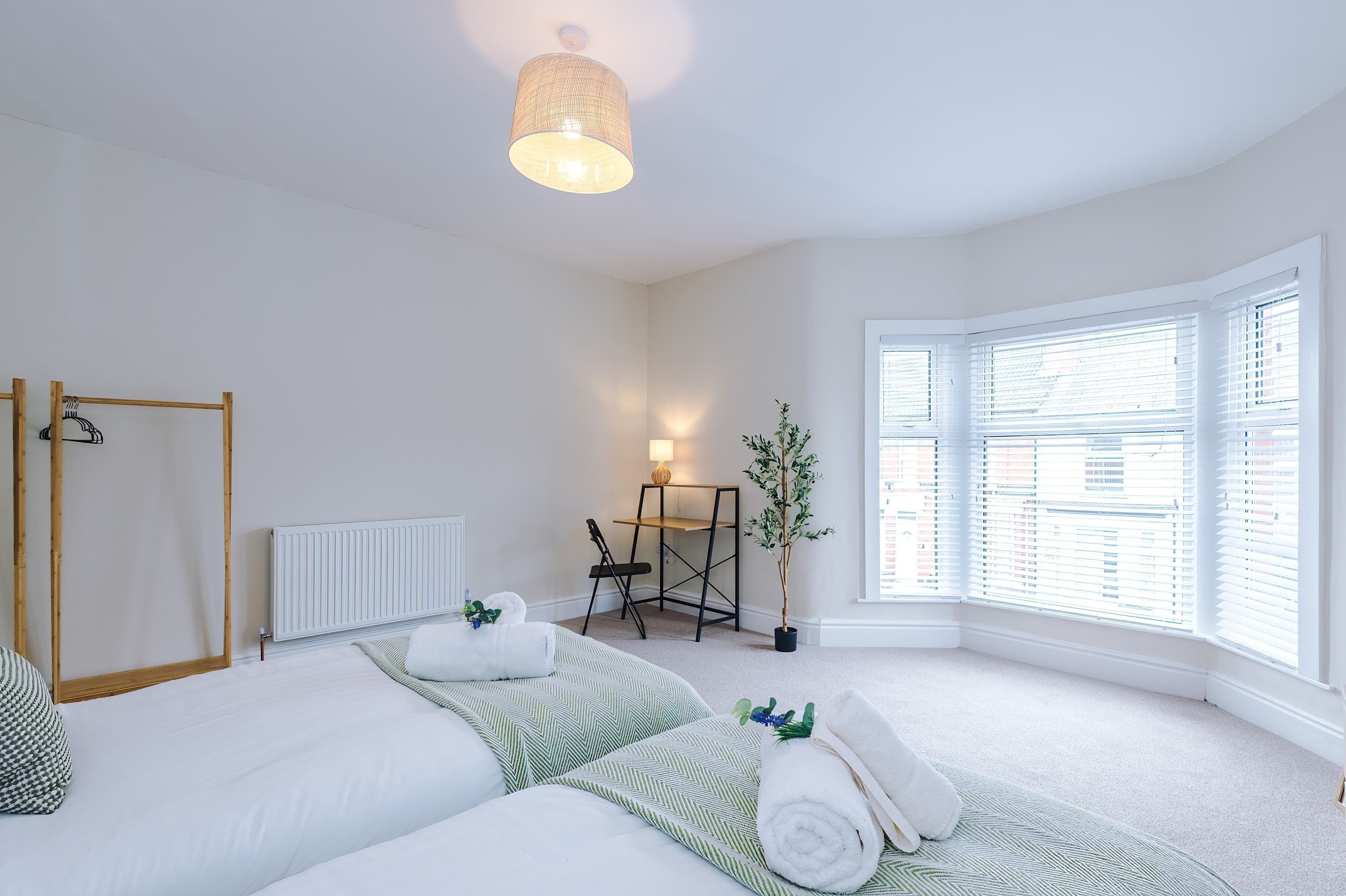 A bedroom with a bed, a bedside table, a chair, a radiator, and a window with blinds.