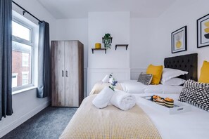 A modern bedroom with a large wardrobe, a bed with white bedding, yellow pillows, and a small shelf with plants. - NEW Spacious Home Ideal for Groups Free Parking (Newcastle-Under-Lyme)