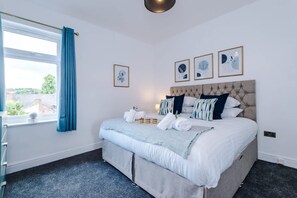A bedroom with a bed, a window with curtains, and framed artwork on the wall. - NEW Spacious Home Ideal for Groups Free Parking (Newcastle-Under-Lyme)