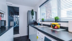 Une cuisine moderne équipée d’un lave-linge encastré, d’un évier et d’une fenêtre avec des stores.