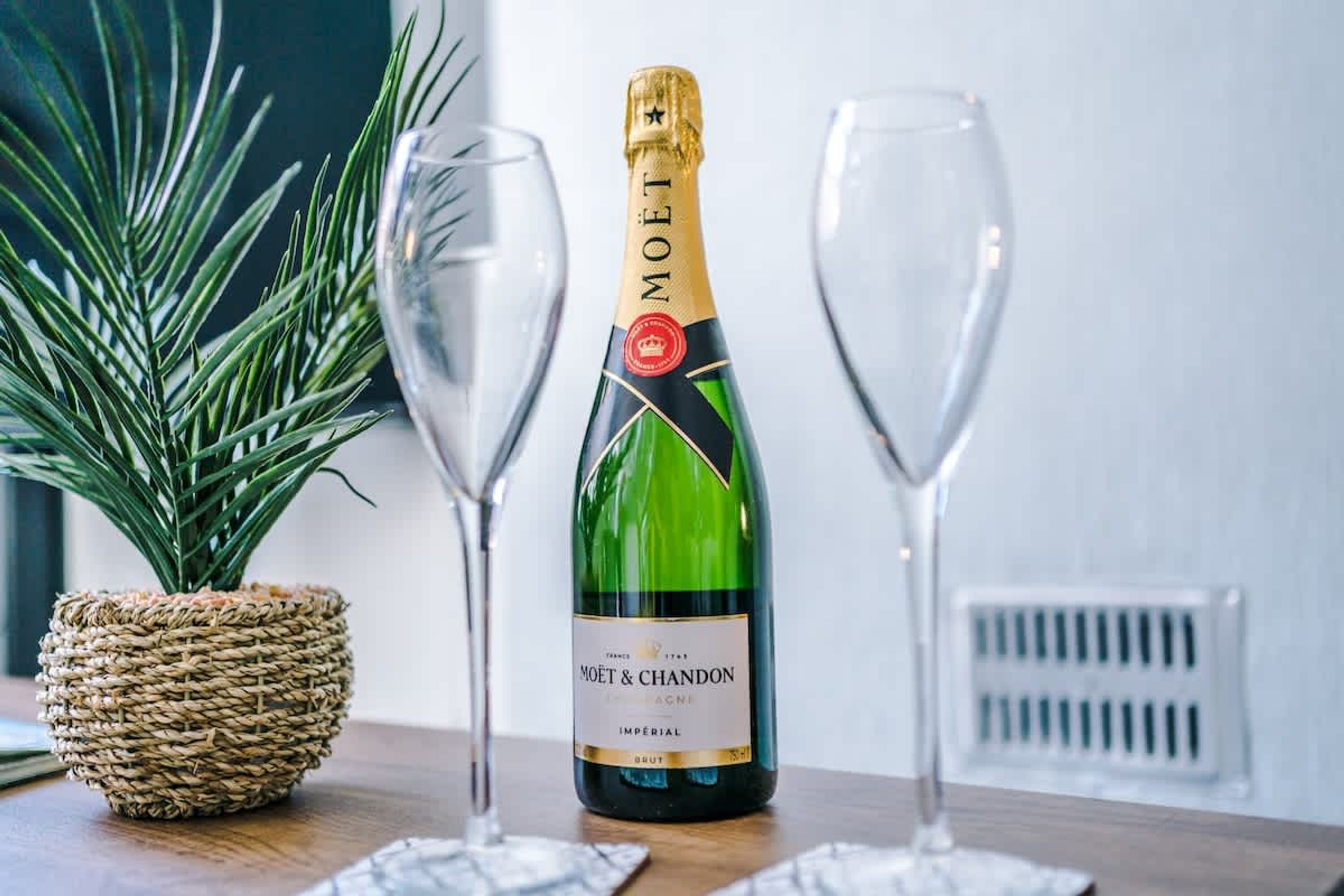 En flaske Moët & Chandon champagne og to glas på et bord med en flettet kurv og en plante.