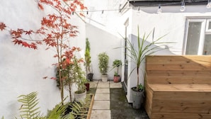 Une petite cour intérieure agrémentée de plantes en pot, d’un banc en bois et d’un mur blanc.