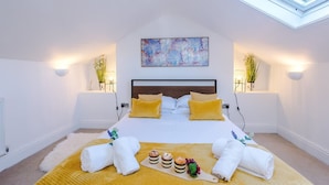 Une chambre d’hôtel moderne avec une lucarne, un grand lit avec des oreillers jaunes, un tableau au-dessus du lit et un plateau de petit-déjeuner posé sur le sol.
