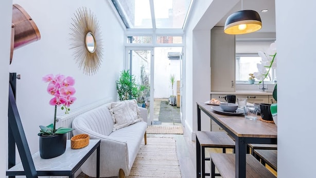 Un intérieur moderne avec un canapé, une table à manger, une suspension et une vue à travers une porte vitrée.