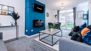 A modern living room with a flat-screen TV, a dining area, and a large window. - Spacious 3-bed Ideal for Long-term Business (Manchester)